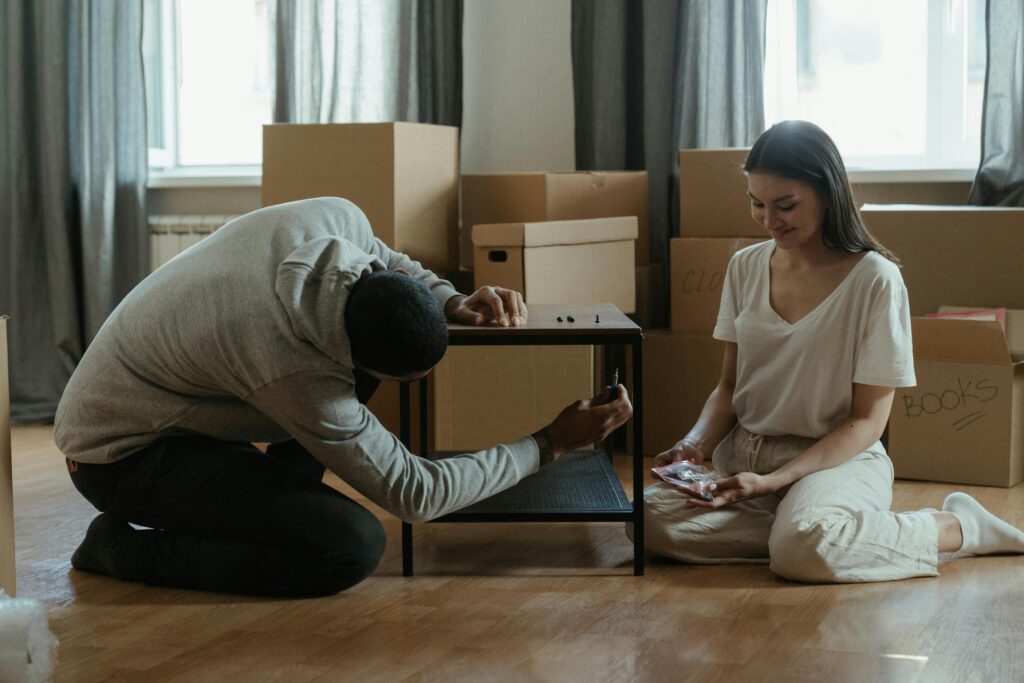 A couple assembling a coffee table amid stacked moving boxes in their new home.